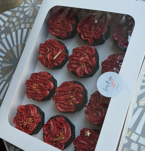 Box of Lovelybakes cupcakes with burgundy frosting and gold sprinkles